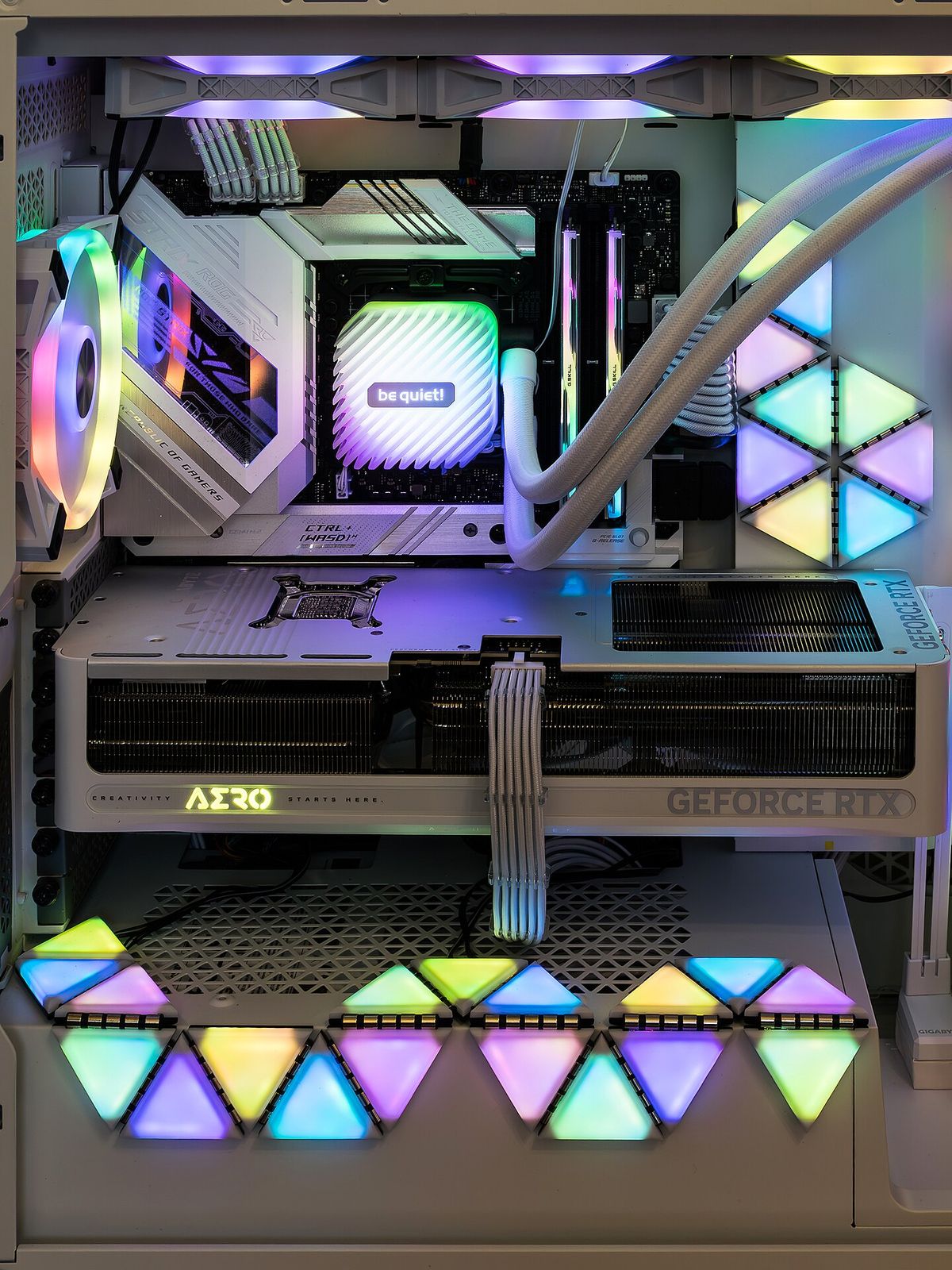 Inside a gaming PC lit in rainbow colours, with a white GeForce RTX graphics card across the middle